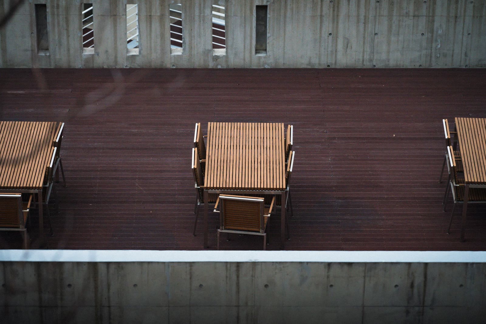 Una terrazza in legno con i tavoli fra muri di cemento